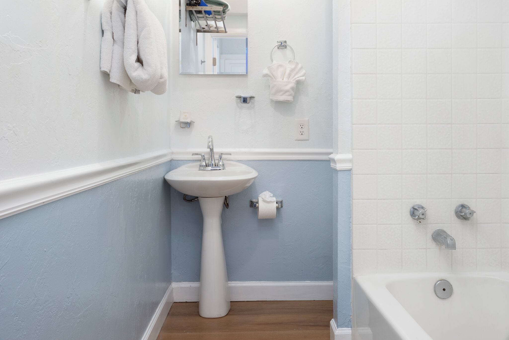 Un bany amb un lavabo de pedestal, una banyera i un mirall sobre el lavabo.