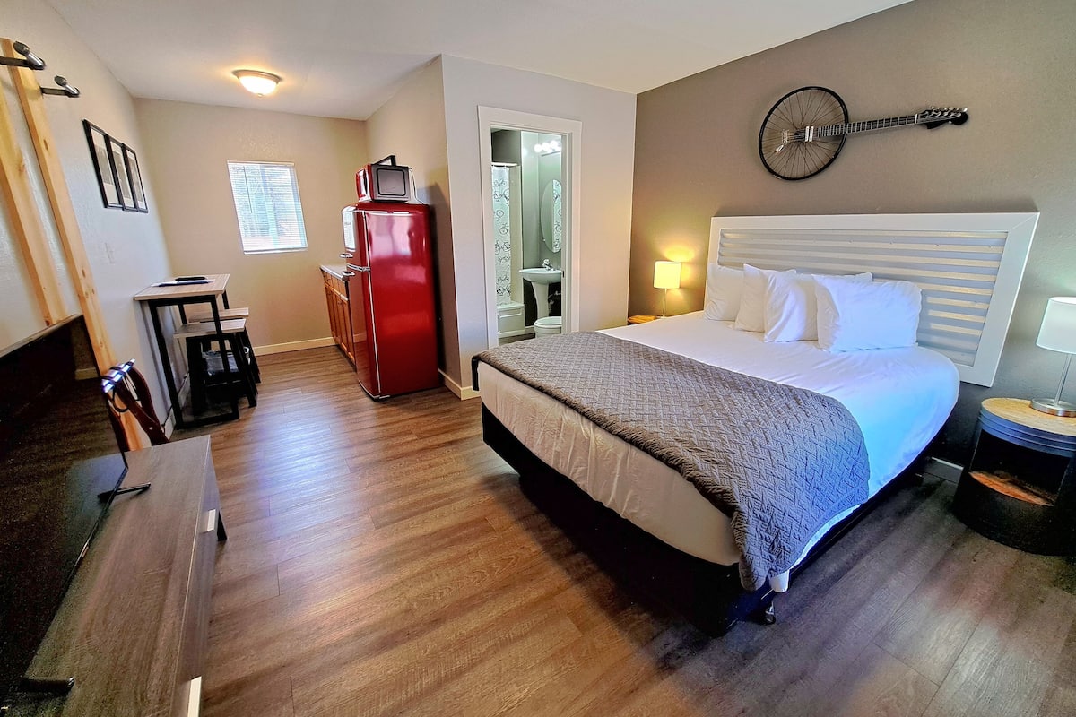 A hotel room with a large bed, a desk, a red refrigerator, a bicycle wall decoration, and a bathroom visible through an open door.