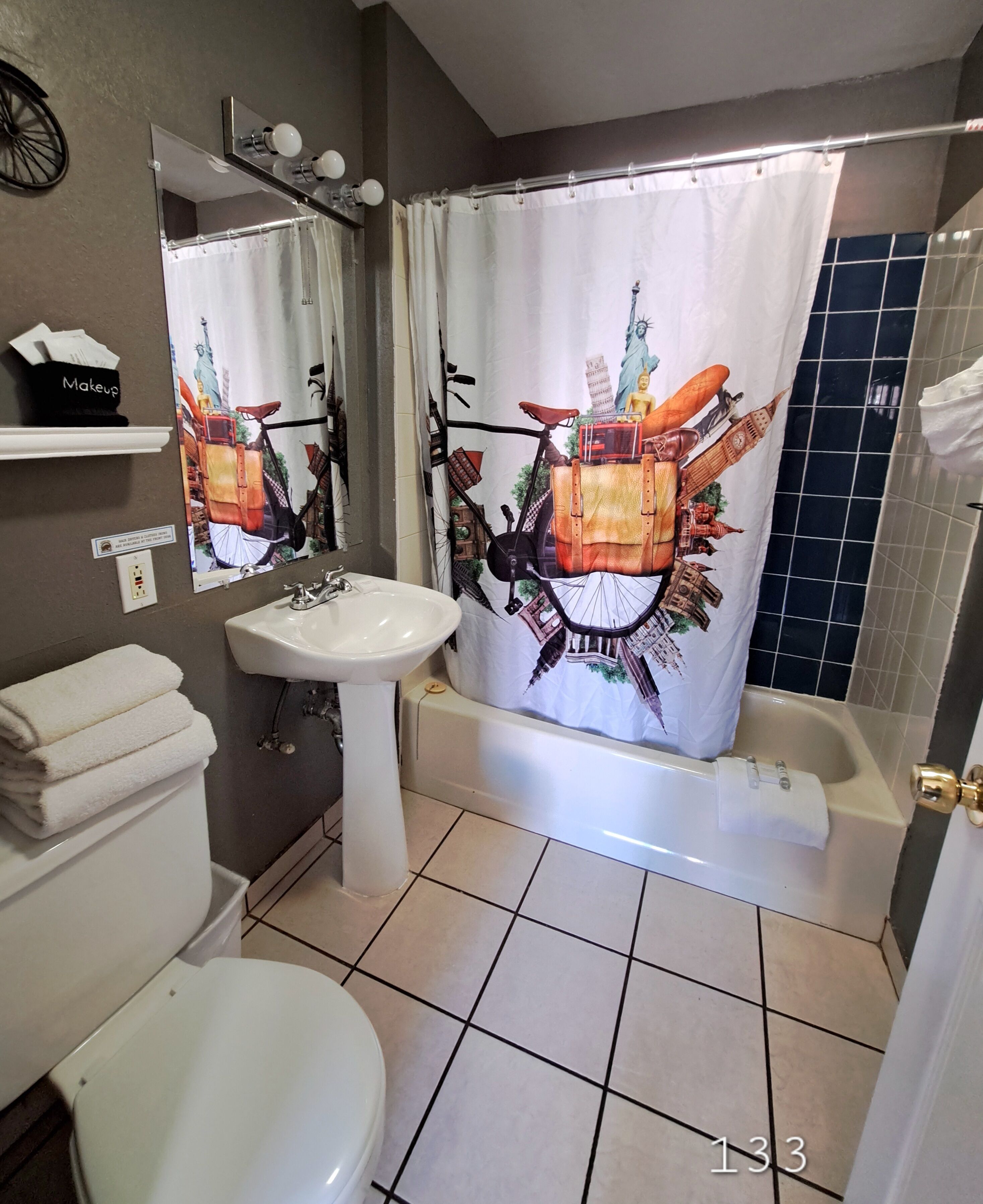 Un baño con lavamanos, inodoro y bañera blancos. Hay un espejo sobre el lavamanos y una cortina de ducha con diseño de paisaje urbano.