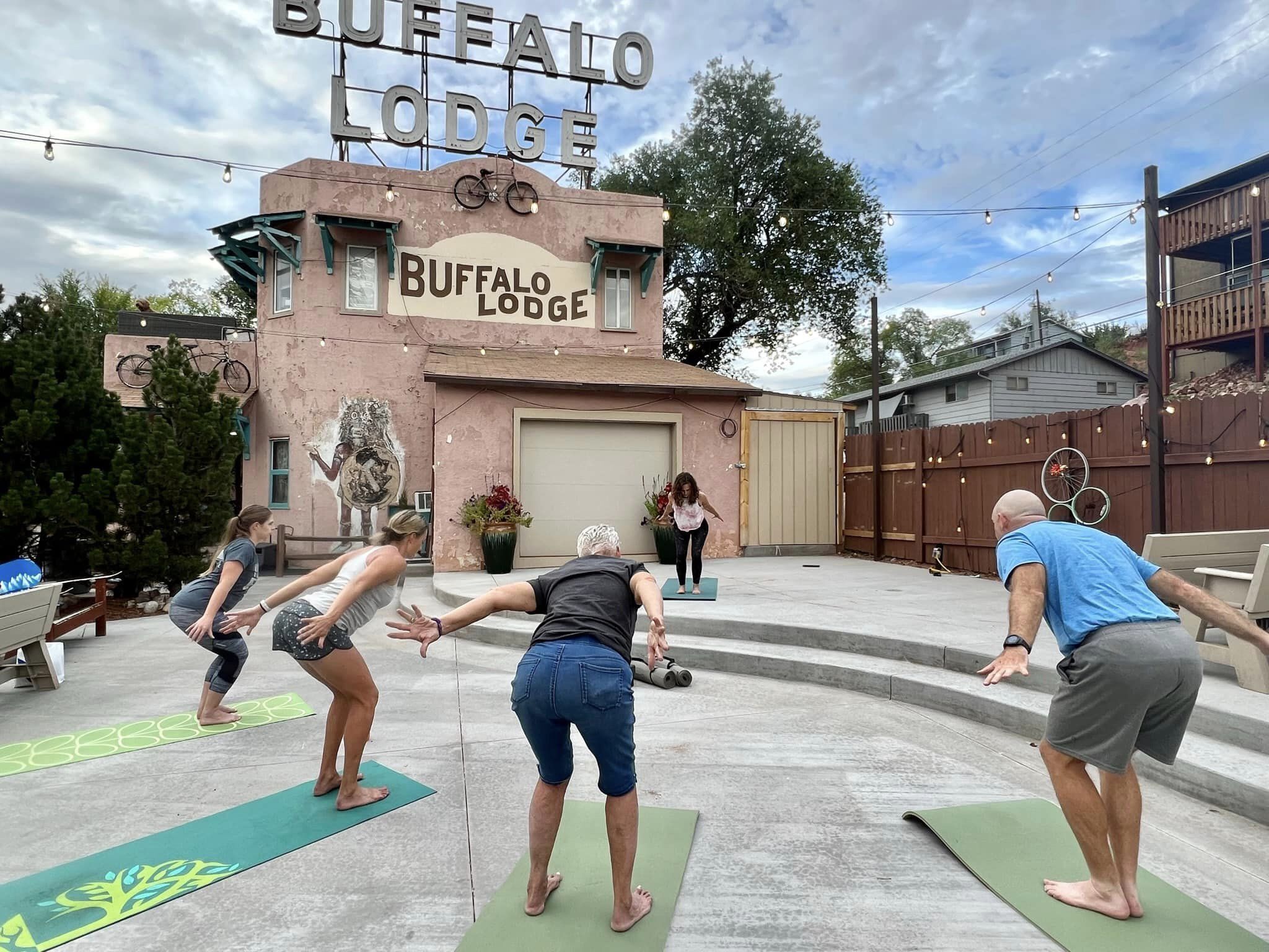 En grupp människor som tränar på yogamattor utomhus, med en byggnad i bakgrunden som har skylten "Buffalo Lodge".