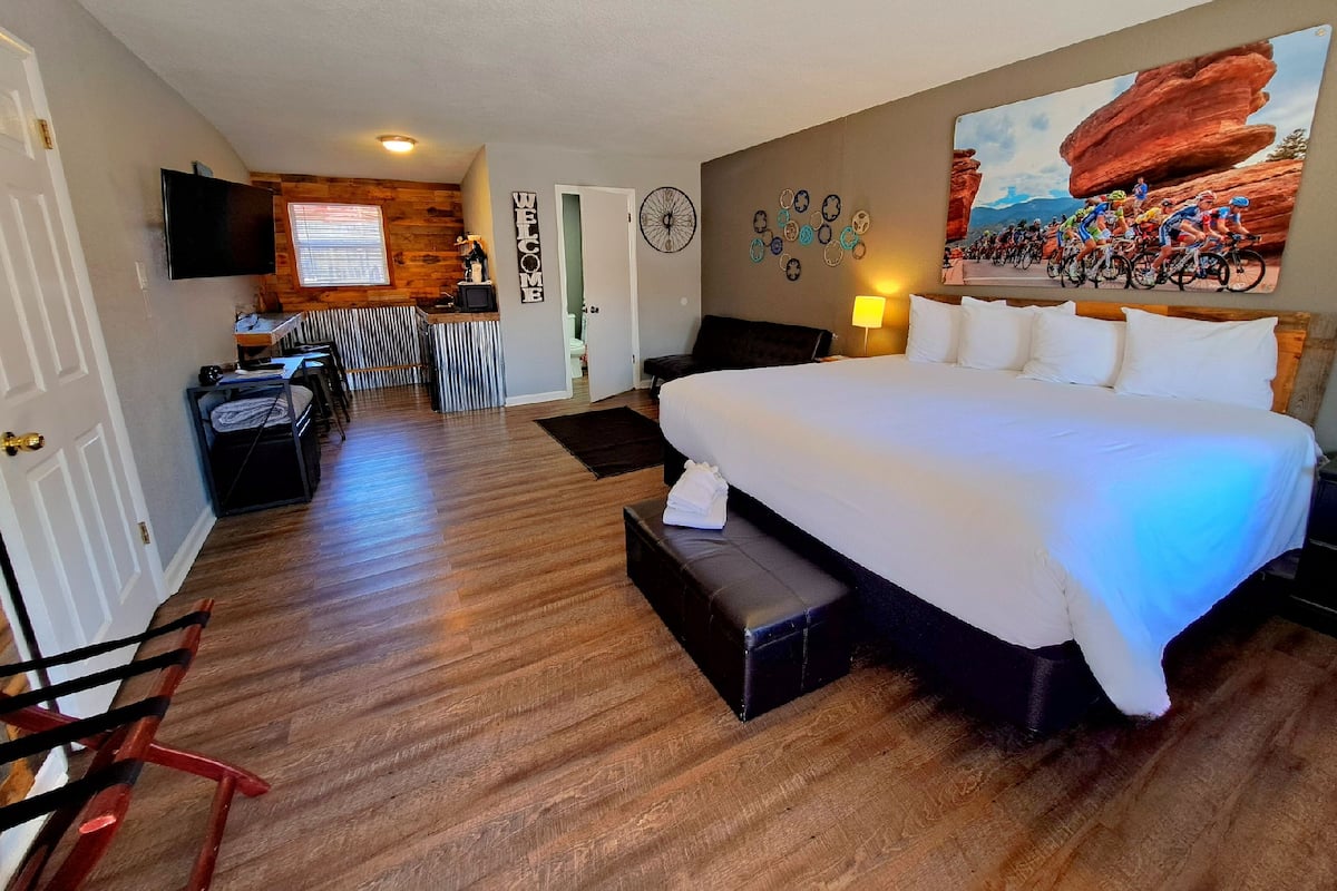 A hotel room with a large bed, a desk with a computer, a TV, and a wall with a cycling race poster.