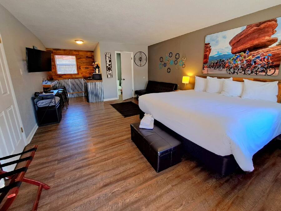 A hotel room with a large bed, a desk with a computer, a TV, and a wall with a cycling race poster.