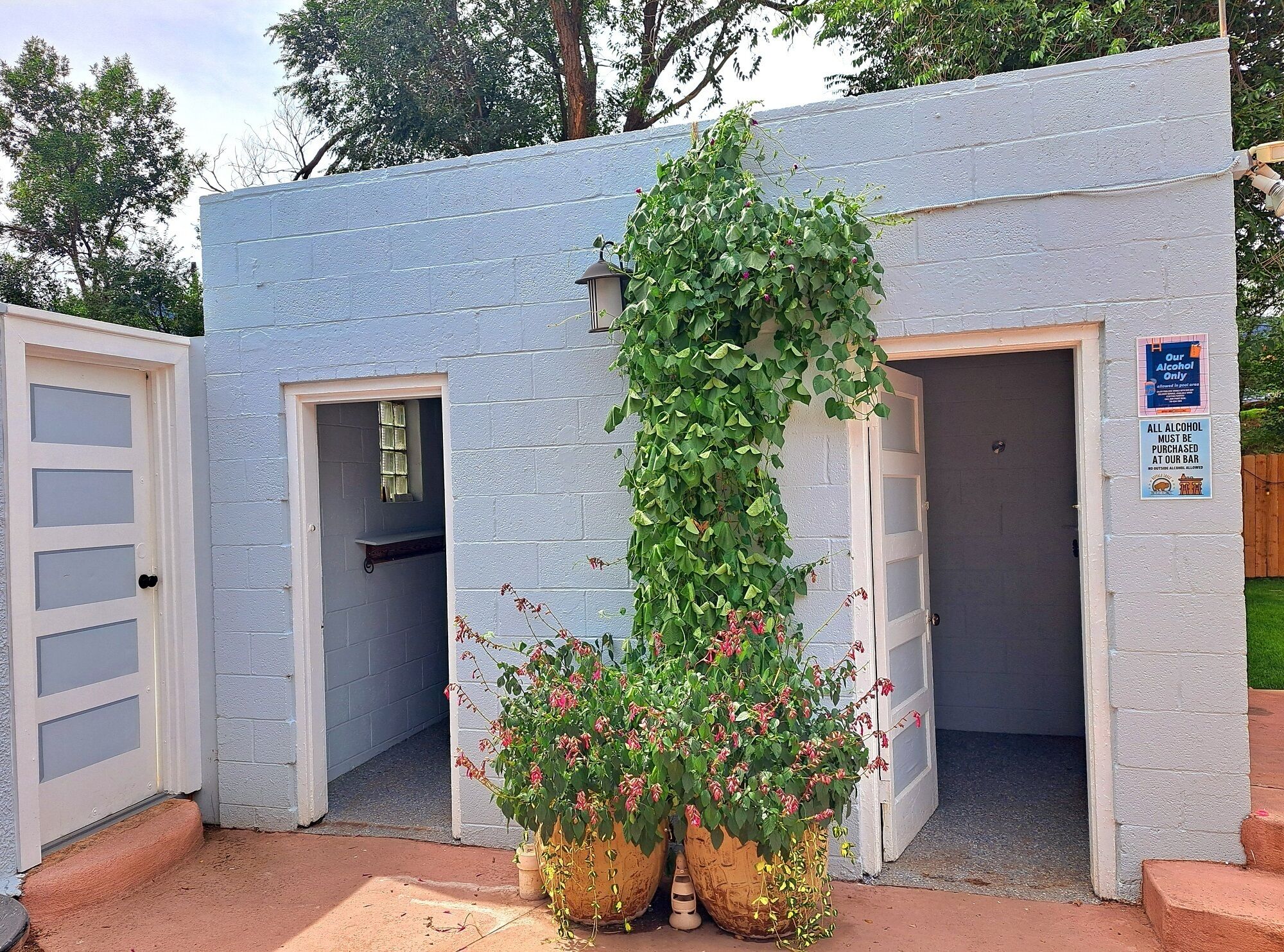 Un petit bâtiment d’un seul étage, doté de deux portes de type garage, d’un pot de fleurs avec des fleurs rouges et d’un panneau indiquant les conditions requises pour l’achat d’alcool.
