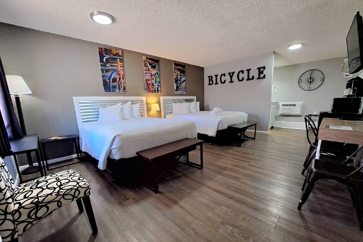 A hotel room with two beds, a bench, a desk, and a bicycle-themed wall.