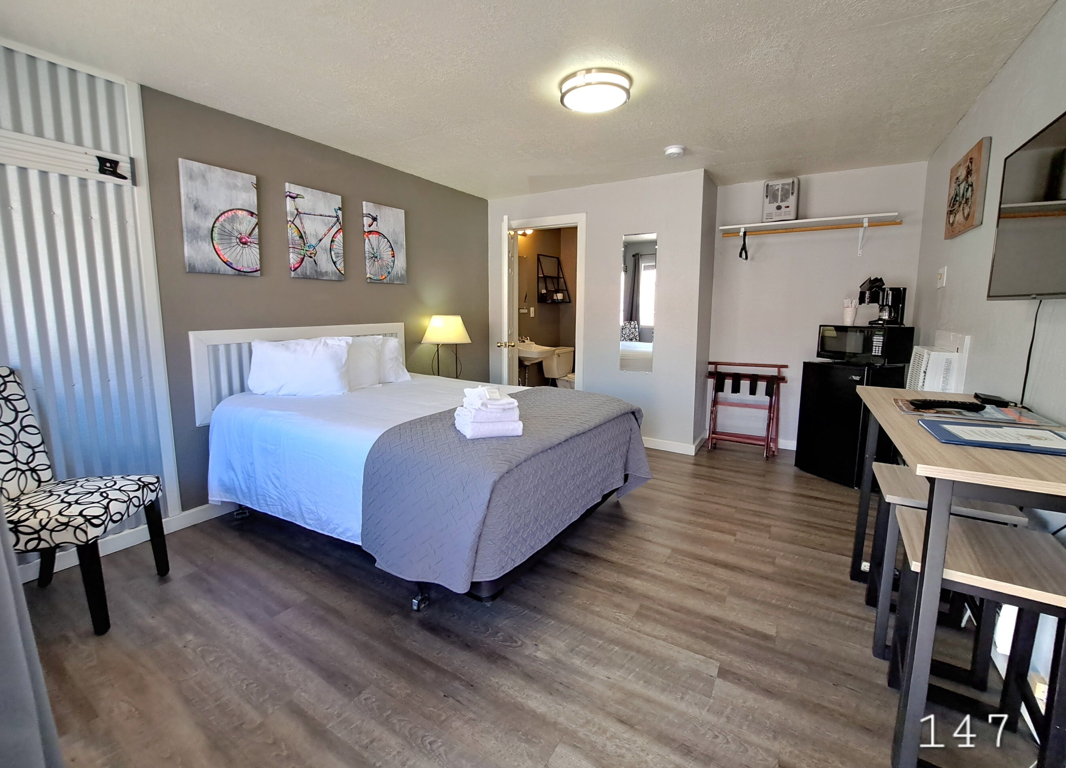 A hotel room with a bed, a chair, a desk, and a kitchenette.