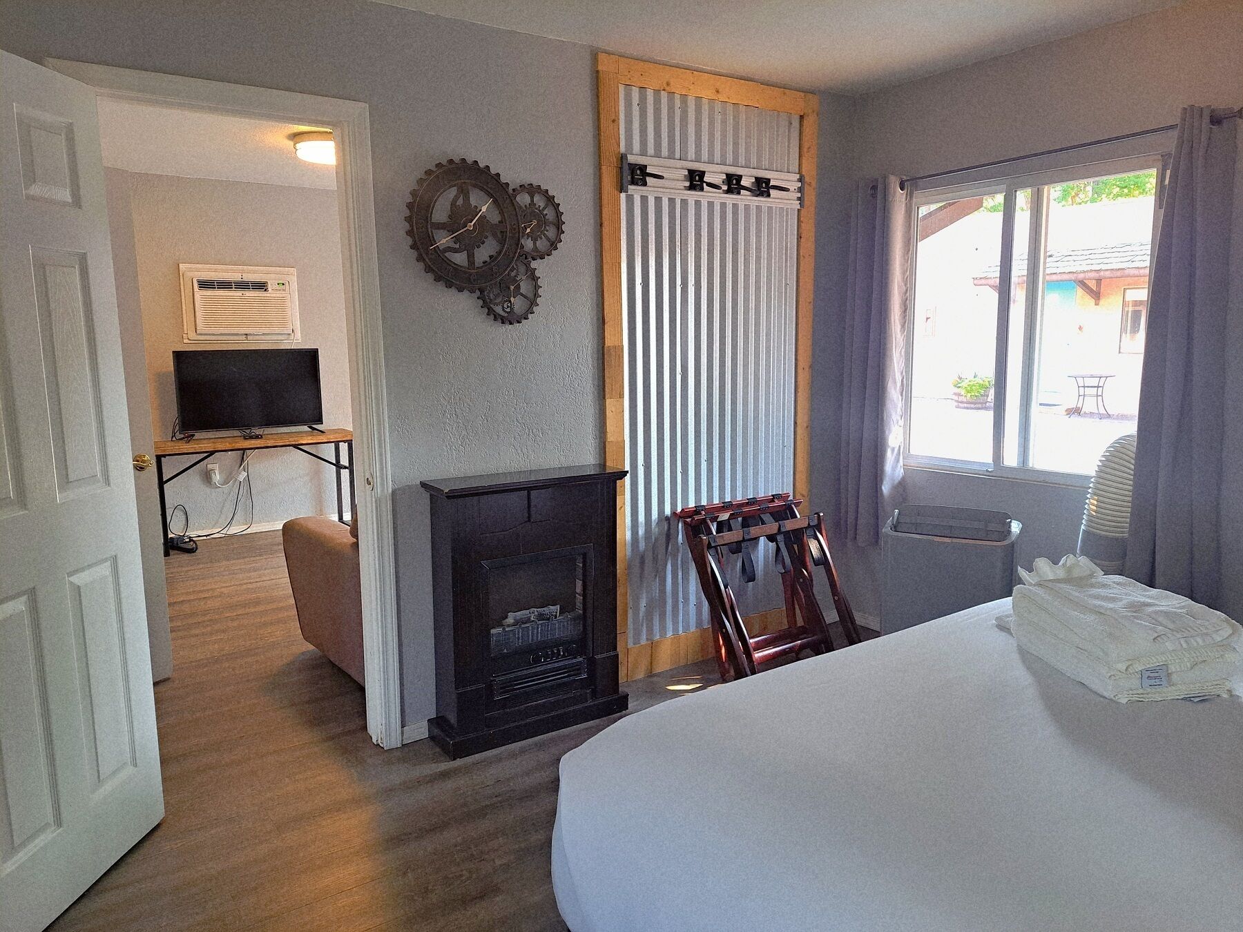 A room with a bed, a fireplace, a television, and a window with curtains.