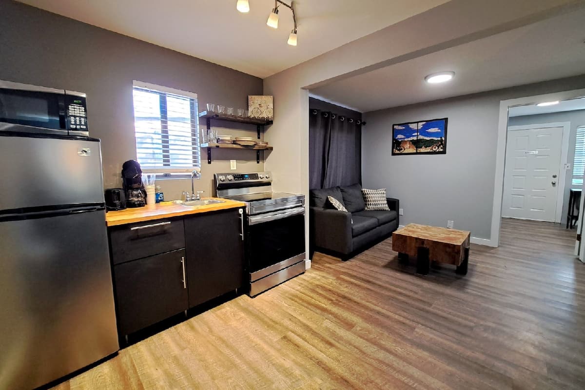 A compact kitchen with modern appliances, a dining area with a wooden table, and a living space with a sofa.
