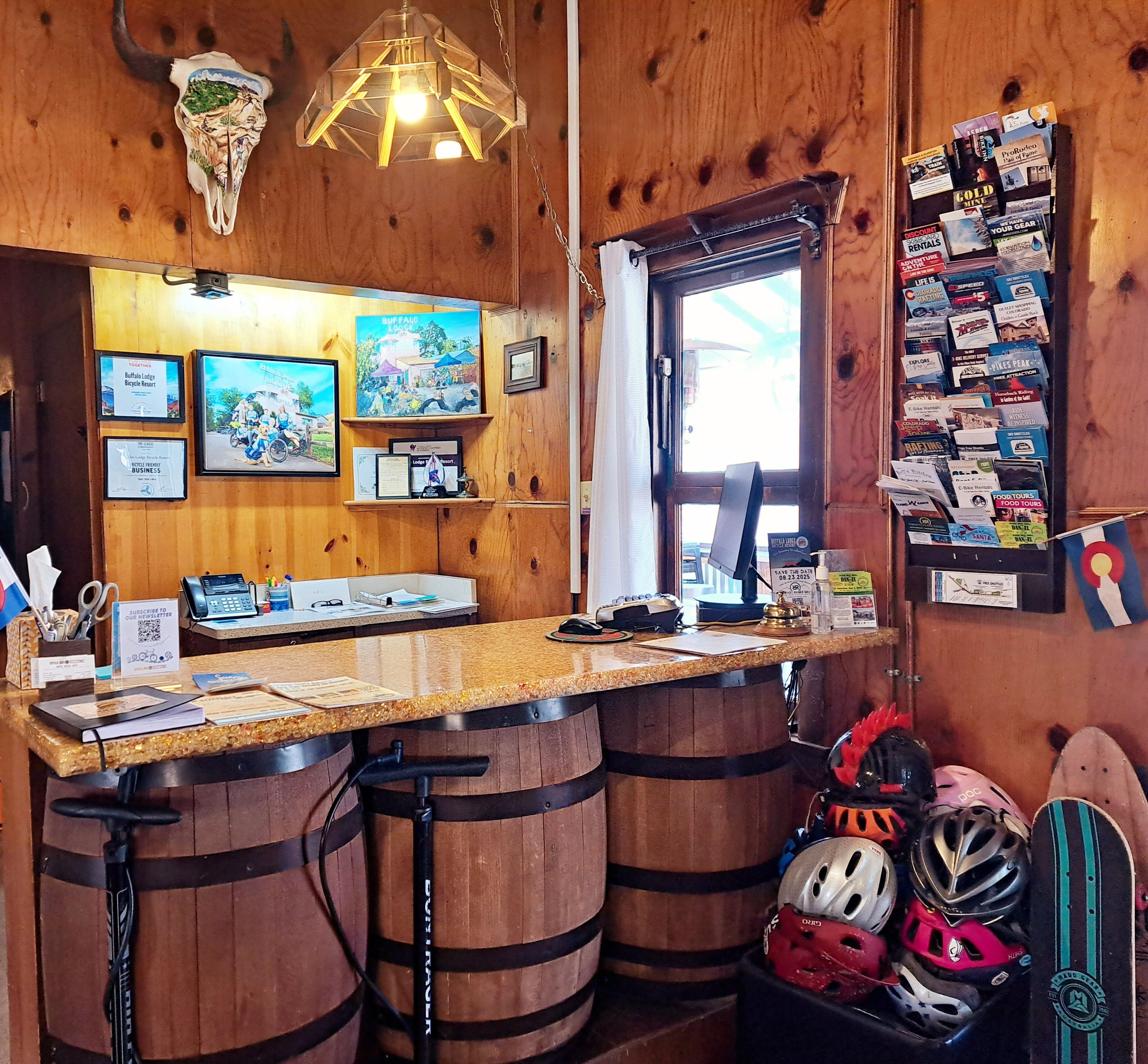 Un rústico espacio de bar con barriles de madera, una barra con distintos objetos, y una pared con cuadros y un tablón de anuncios.