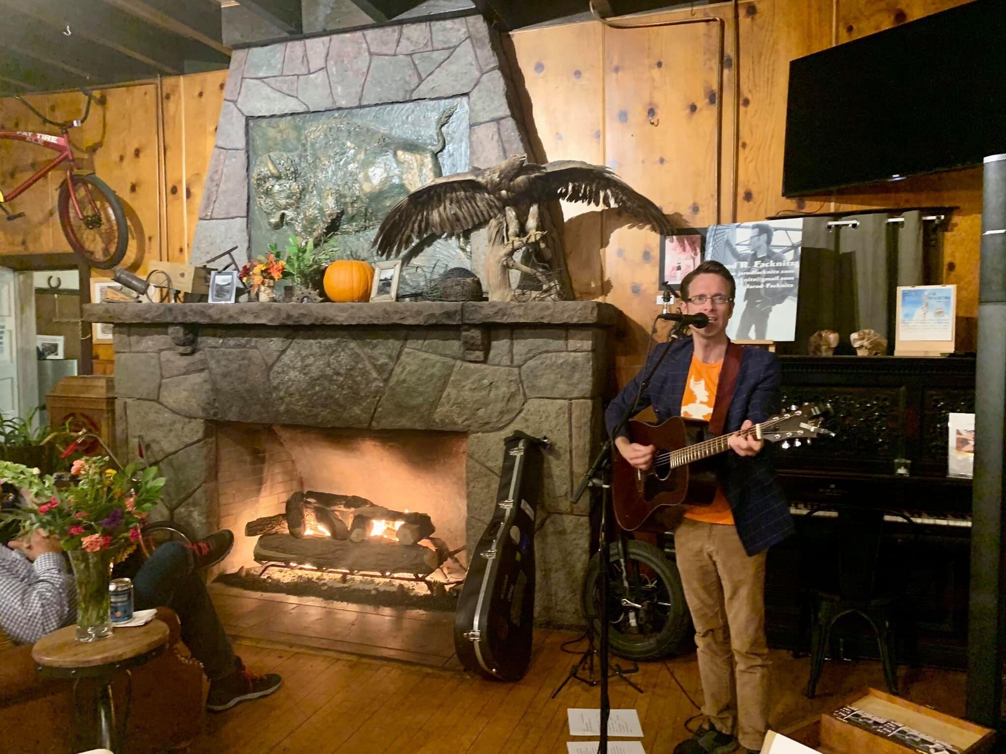 Une pièce chaleureuse avec une cheminée en pierre, un guitariste et une décoration rustique.