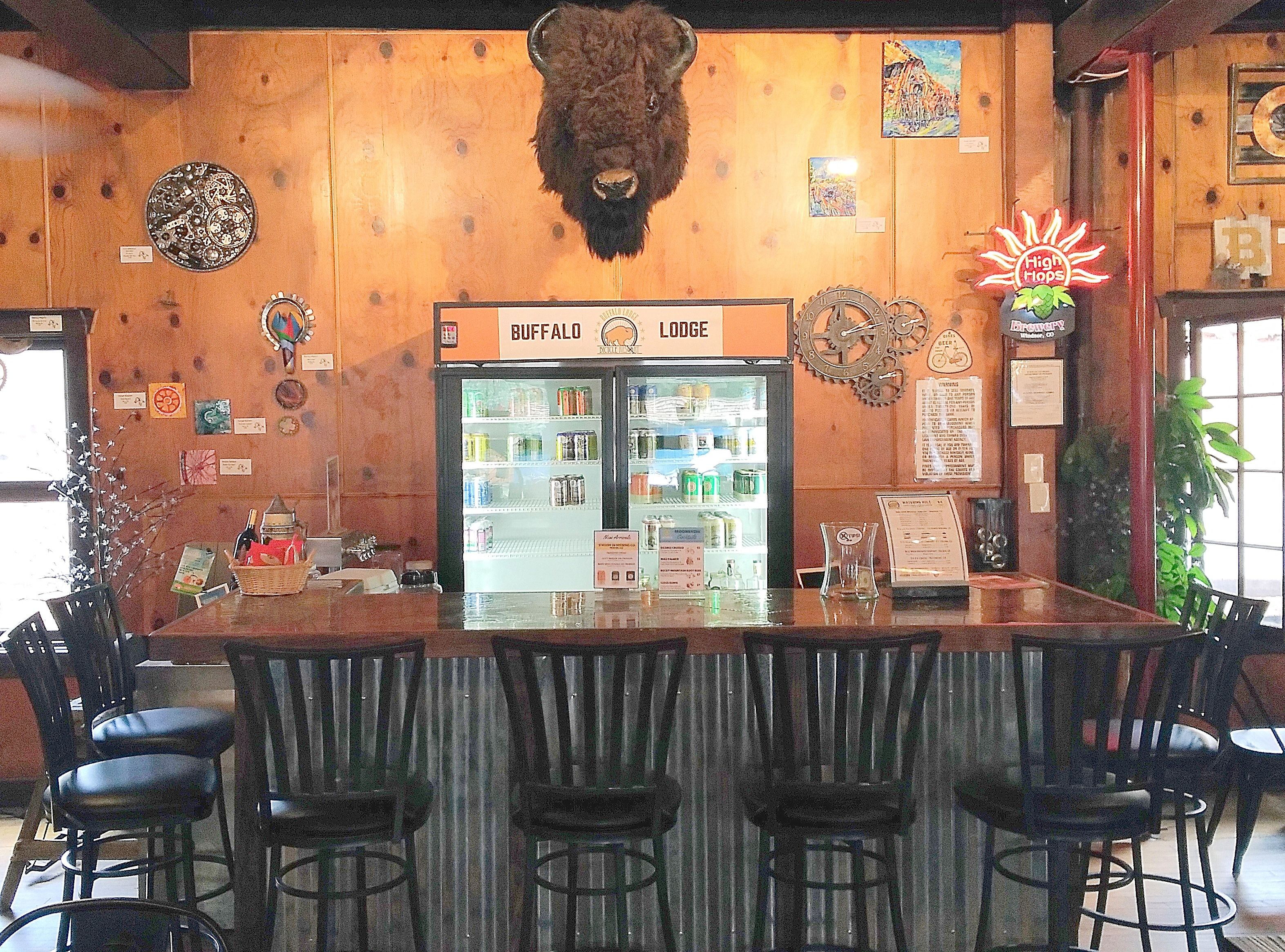 A bar area with a buffalo head decoration, a refrigerator stocked with beverages, and a sign reading "BUFFALO LODGE".