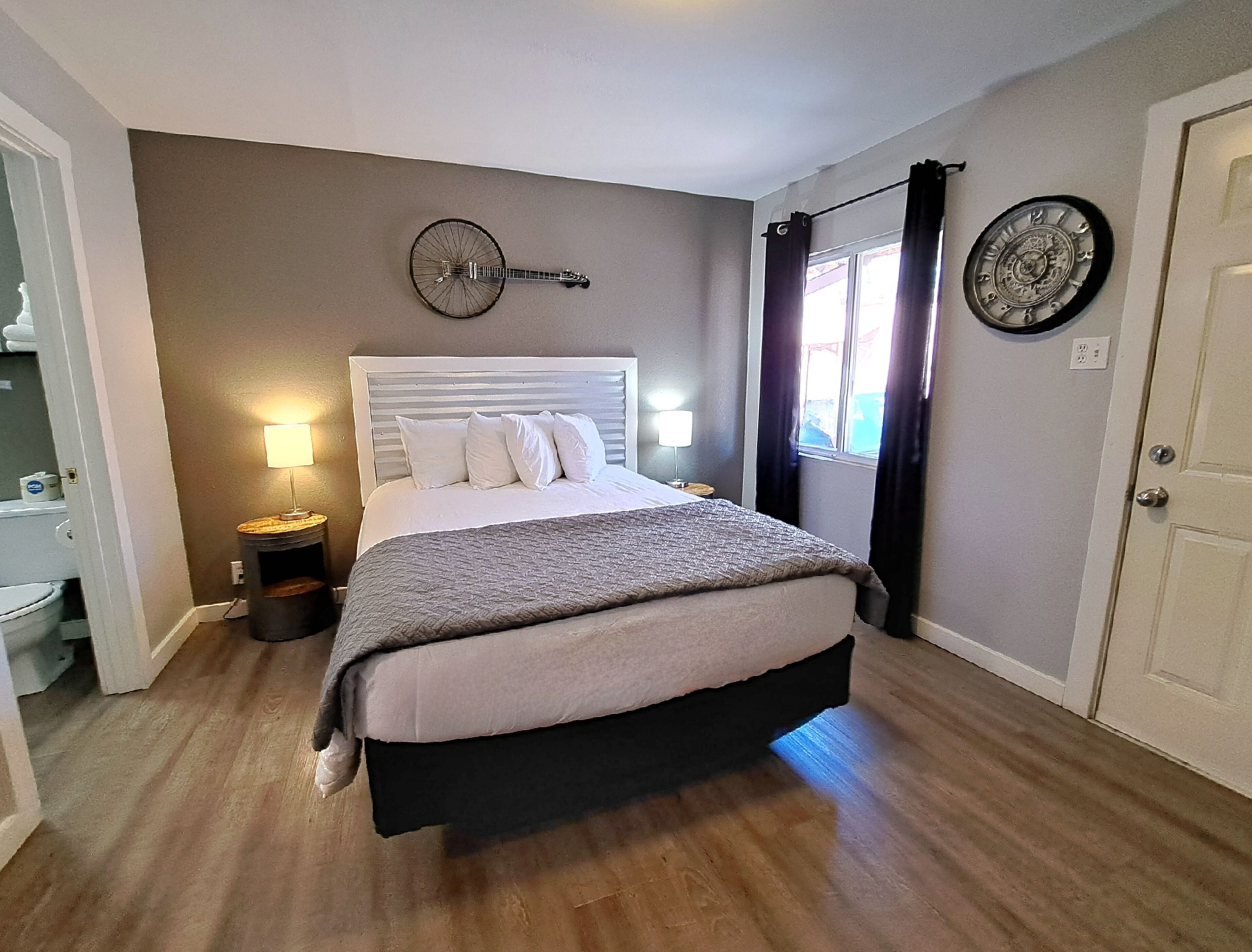 A bedroom with a bed, bedside lamps, a clock on the wall, and a door.