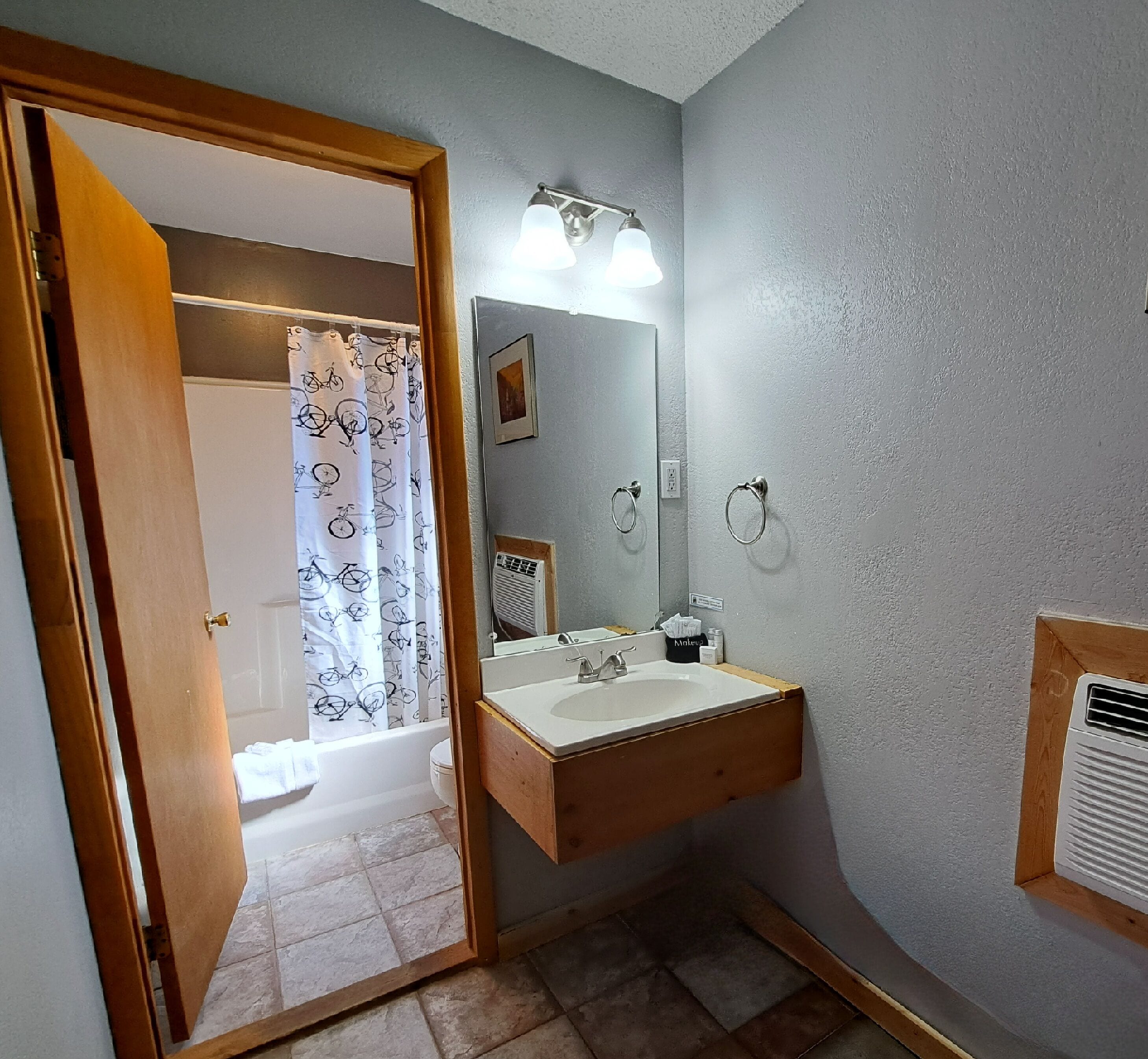 Un baño con tocador de madera, un lavamanos, un espejo y una ducha con cortina de estampado de bicicleta.