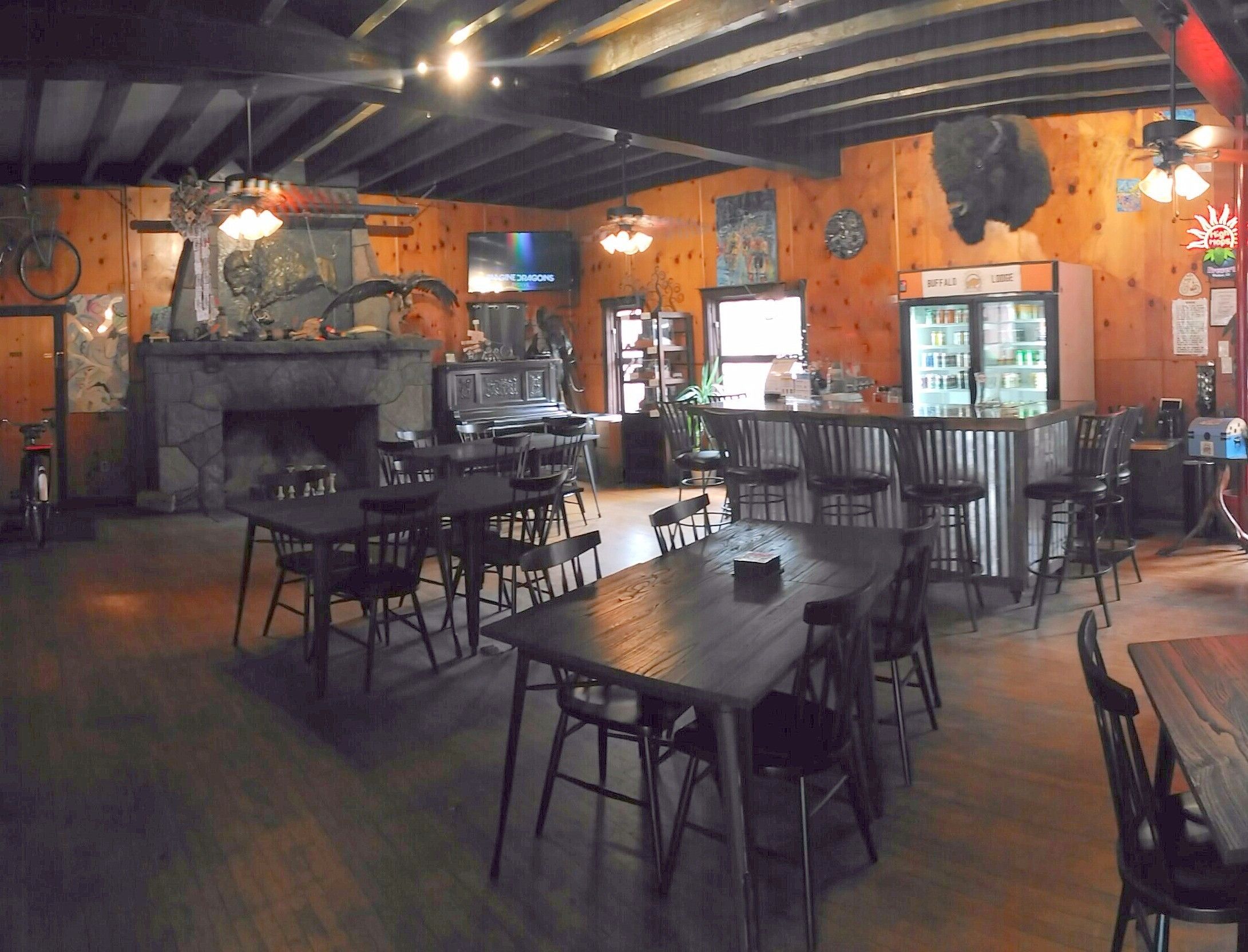 A restaurant interior with wooden walls, a stone fireplace, and a bar area.