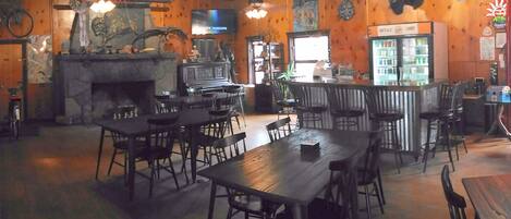 A restaurant interior with wooden walls, a stone fireplace, and a bar area.