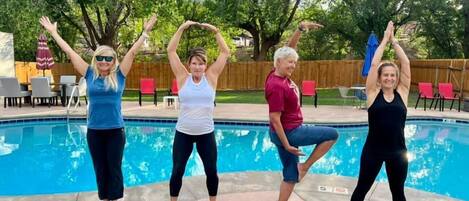 Quatre personnes pratiquent des postures de yoga au bord d’une piscine.
