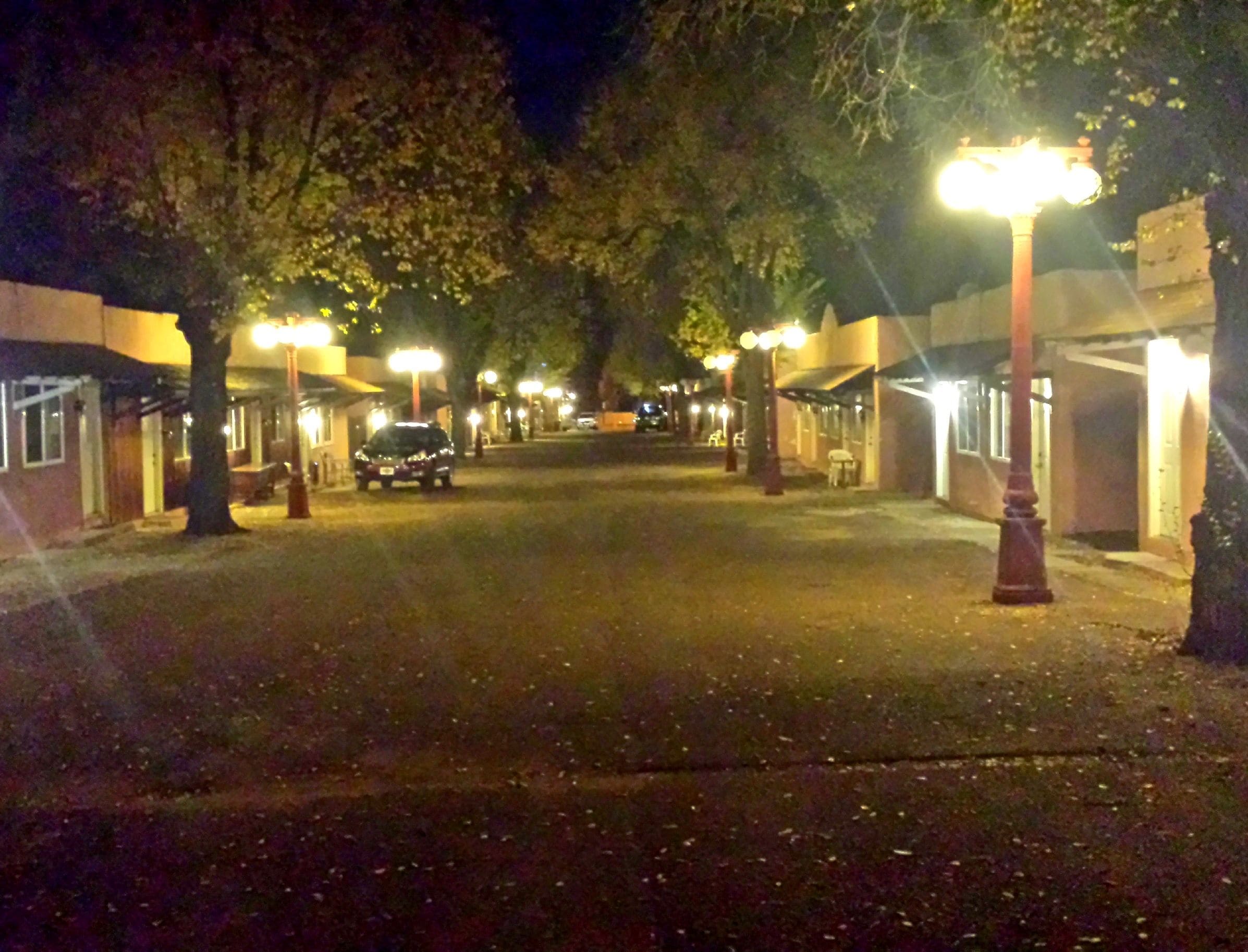 A nighttime street scene with buildings on either side, street lamps, and a parked car.