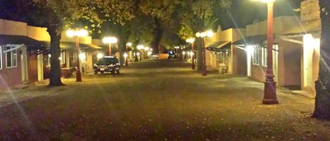 A nighttime street scene with buildings on either side, street lamps, and a parked car.