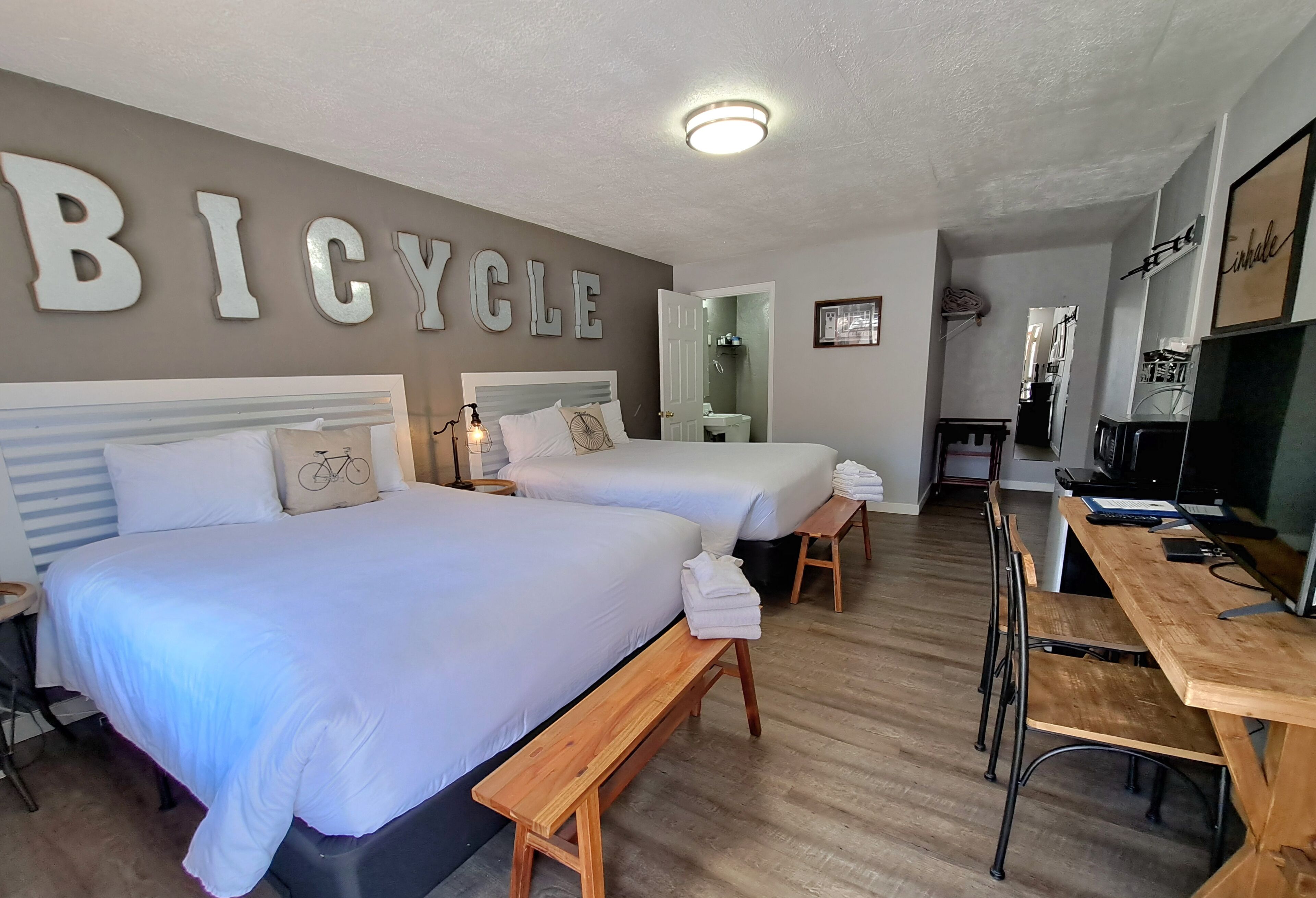 A hotel room with two beds, a wooden bench, a desk, and a mirror.