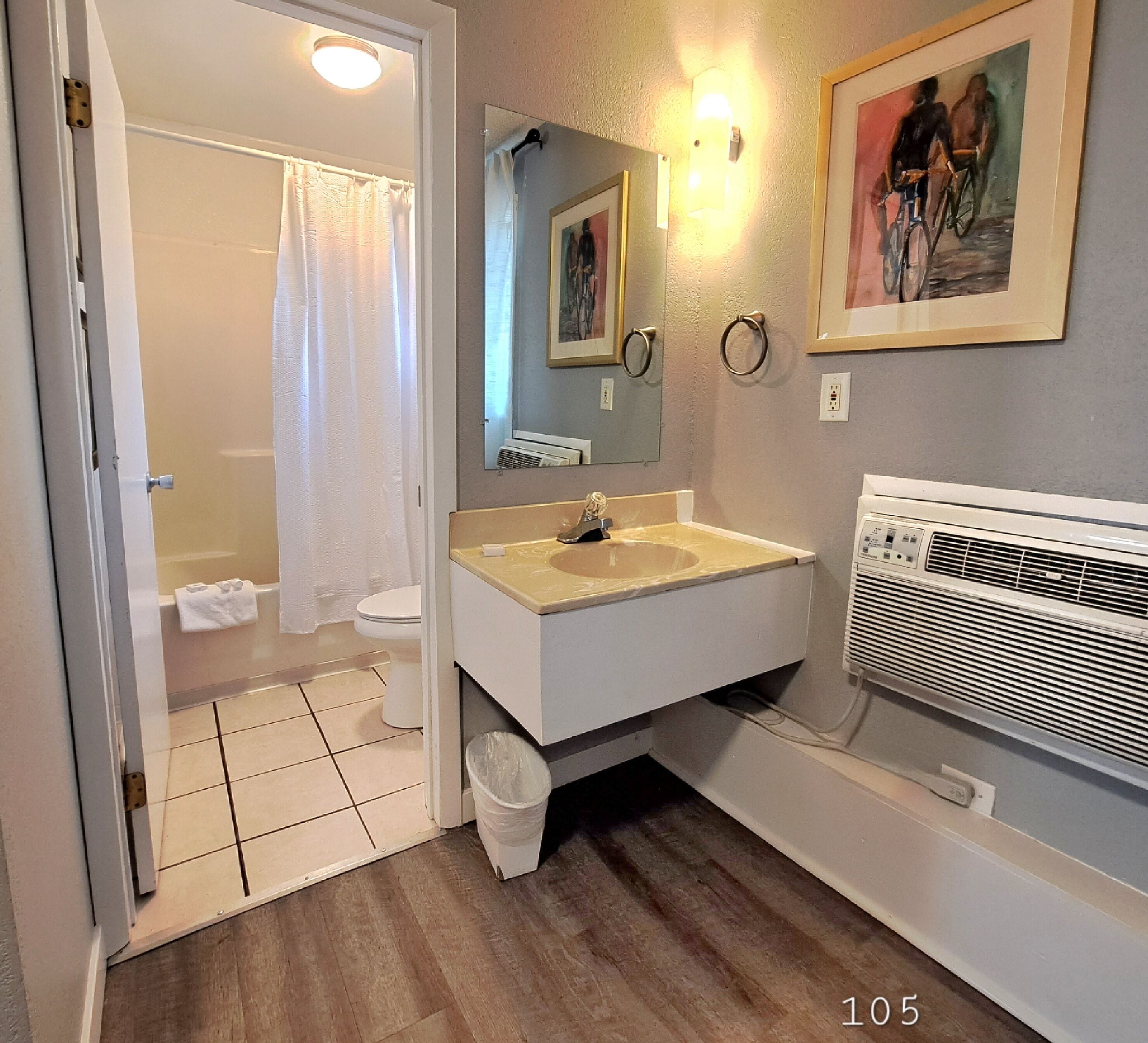 A bathroom with a toilet, sink, mirror, and shower.