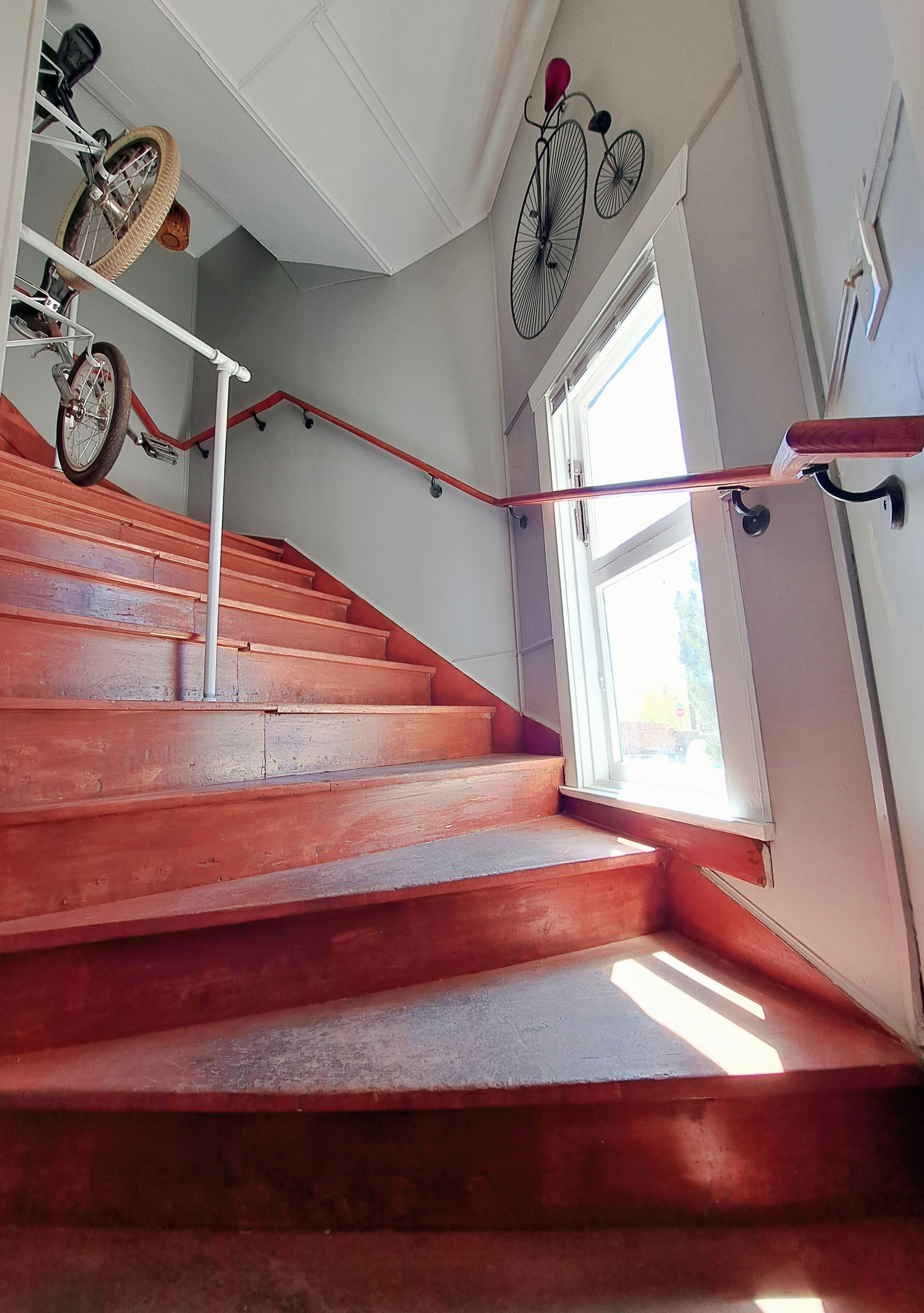 A staircase with wooden steps and a handrail, leading to a landing with a window and a bicycle rack.