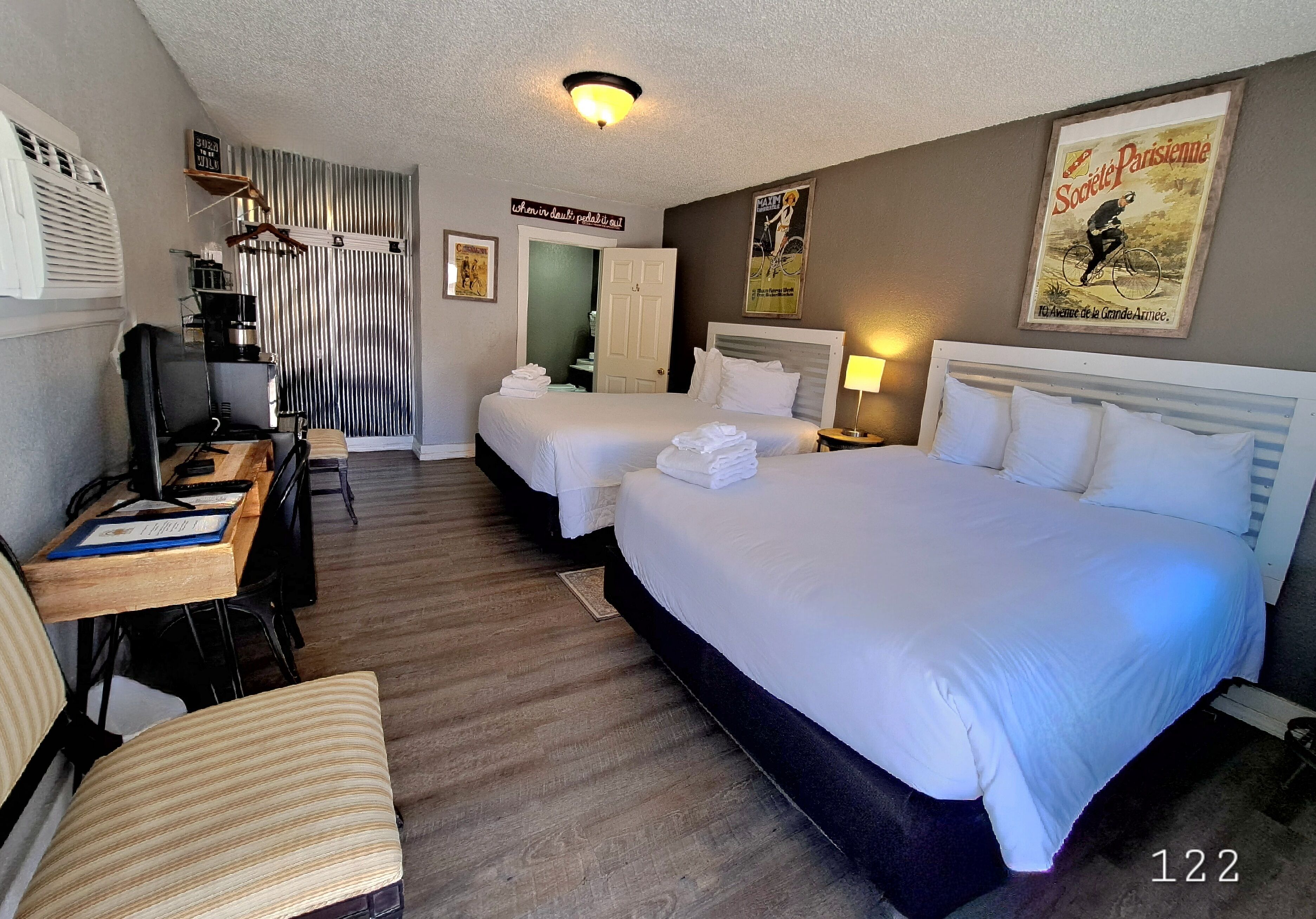 A hotel room with two beds, a desk with a chair, a coffee machine, and a wardrobe.