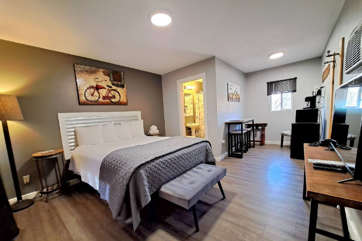 A modern bedroom with a large bed, a bench, a desk, and a bicycle painting on the wall.