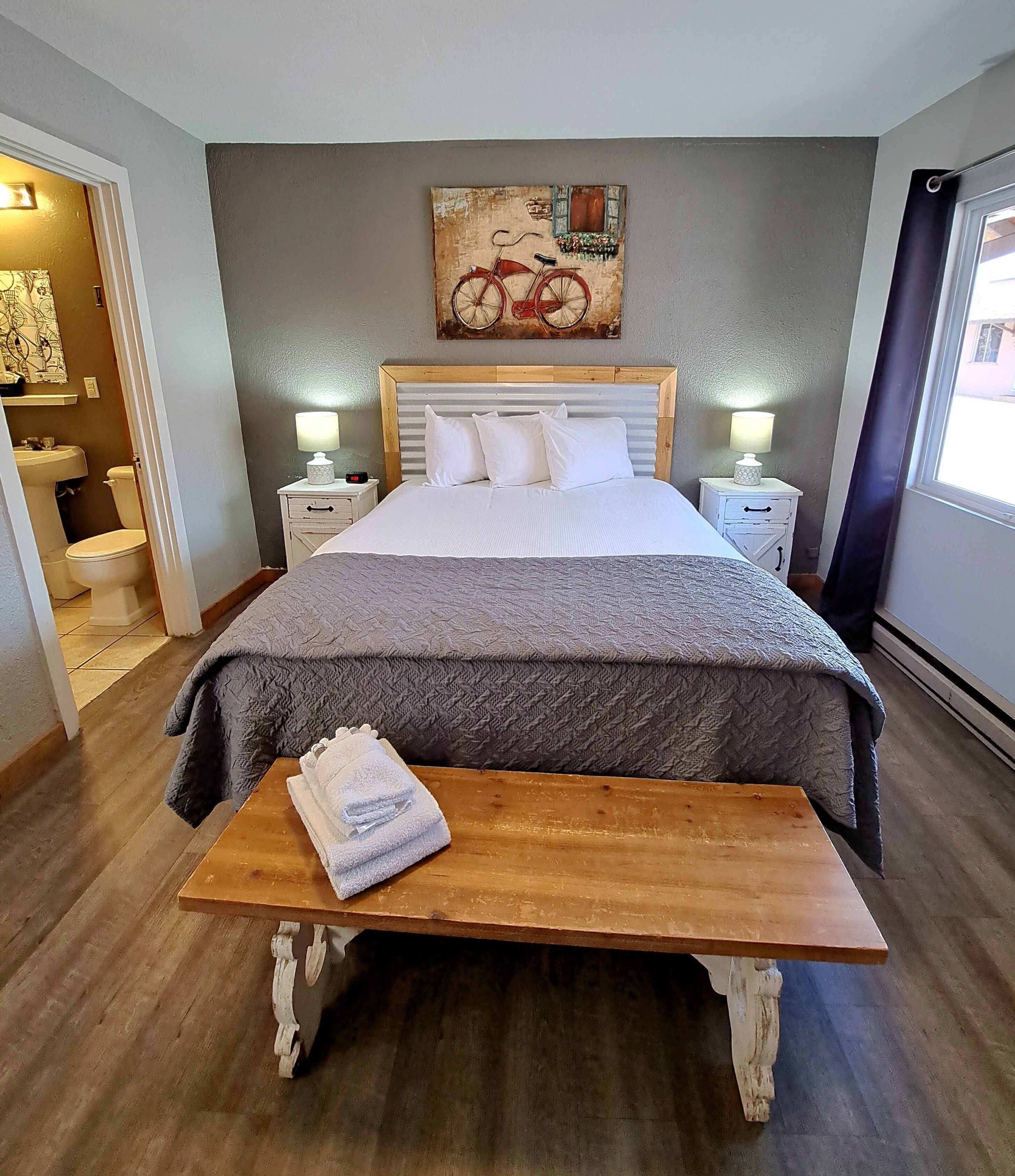 A neatly arranged bedroom with a bed, bedside tables, a bench, and a painting on the wall.