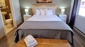 A neatly arranged bedroom with a bed, bedside tables, a bench, and a painting on the wall.