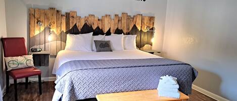 A bedroom with a bed, a chair, a wooden headboard, and a wall sign that reads "THE MOUNTAINS ARE CALLING".