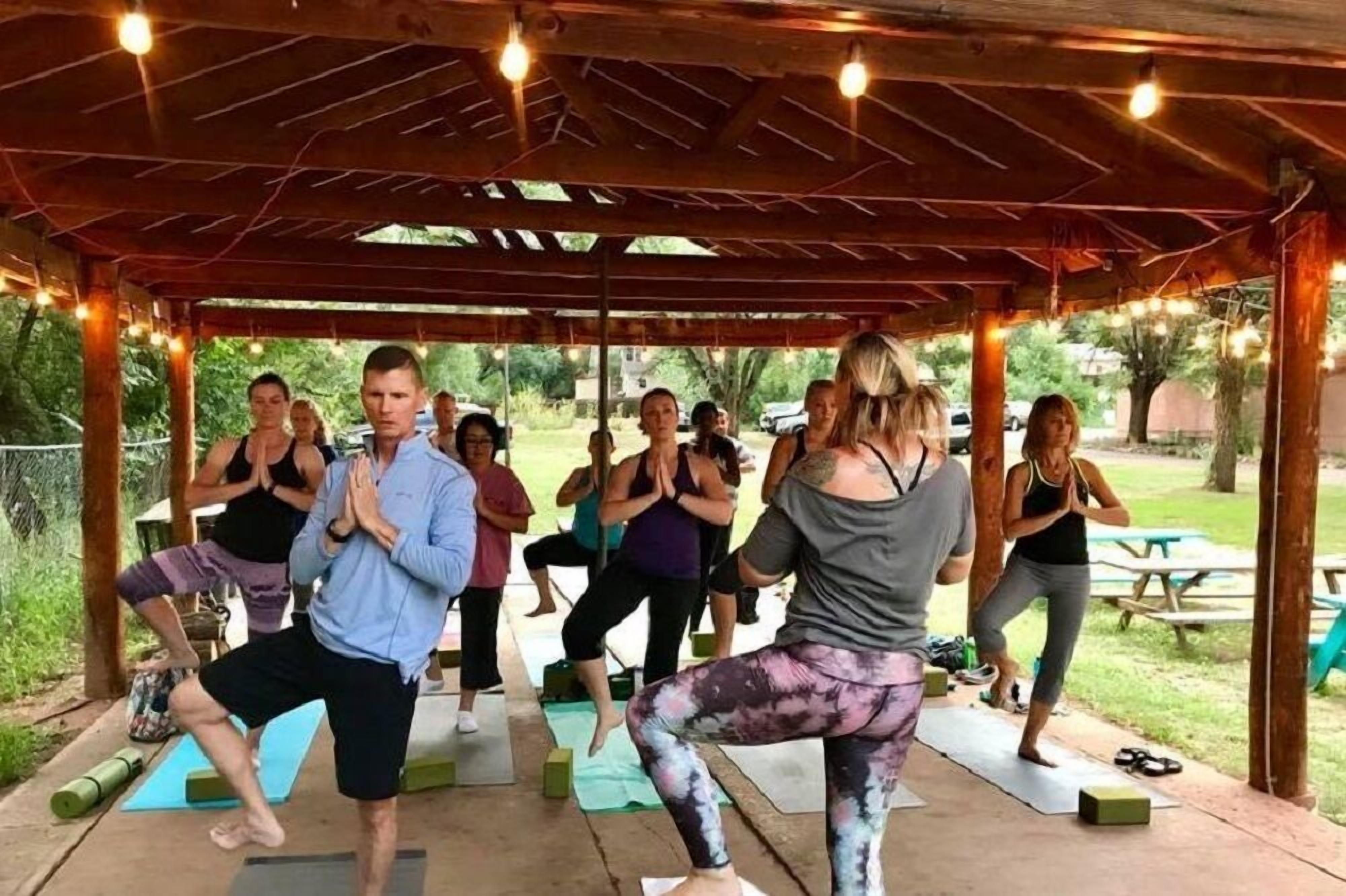 A group of people performing yoga under a wooden gazebo with string lights.