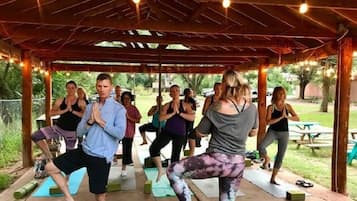 A group of people performing yoga under a wooden gazebo with string lights.