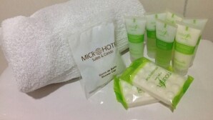 A white towel, a white bag with text, and several green and white bottles on a white surface. - Micro Hotel Condo Suites (Santo Domingo)