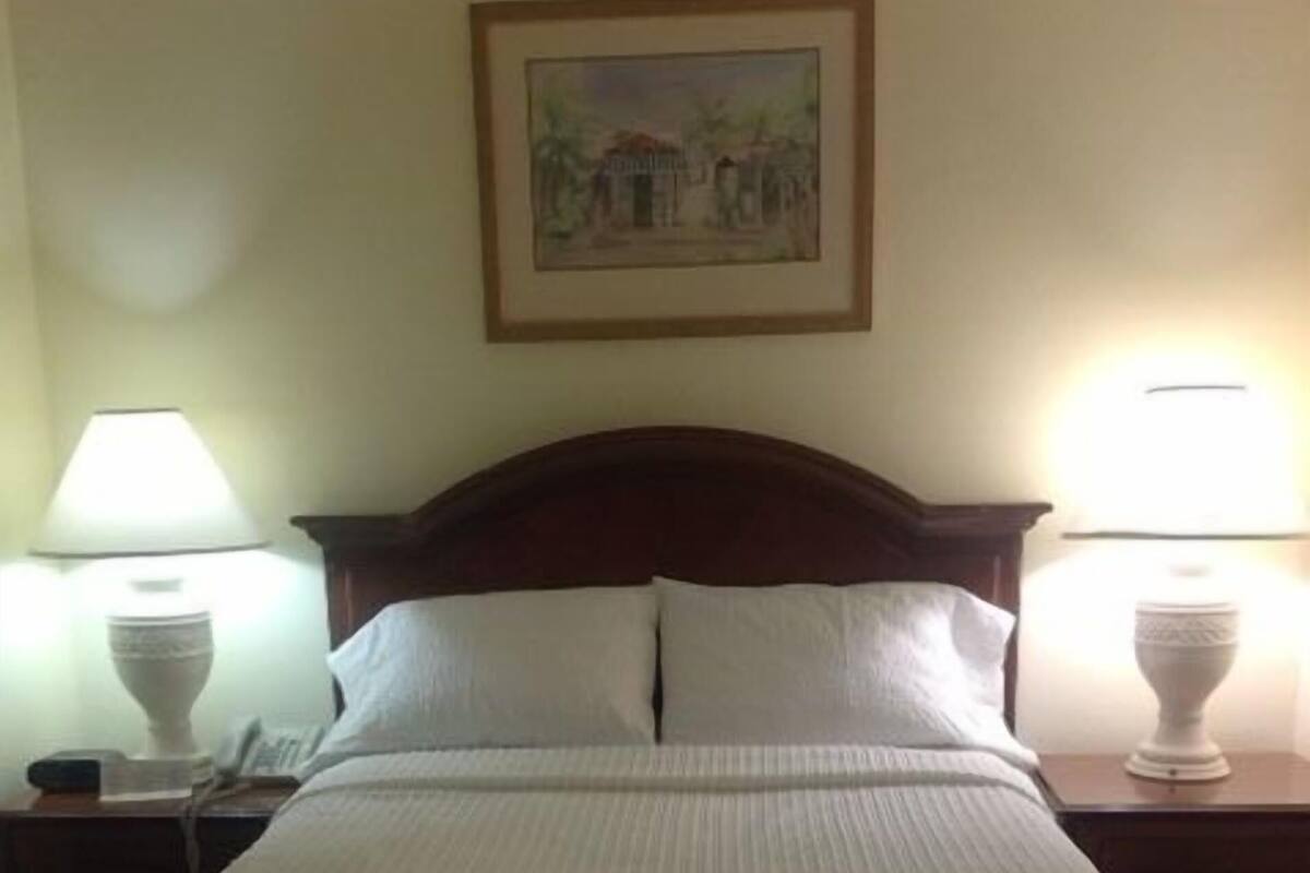A bed with a wooden headboard, two bedside tables with lamps, and a framed picture on the wall.