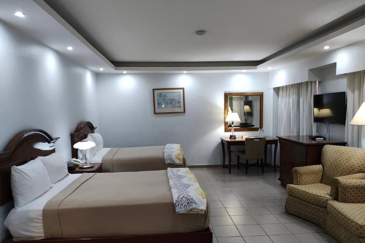 A hotel room with two beds, a desk, a chair, a television, and a mirror.