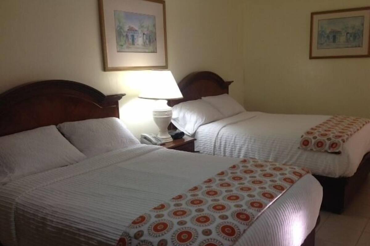 A hotel room with two beds, a nightstand with a lamp, and two framed pictures on the wall.