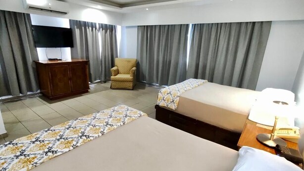 A hotel room with two beds, a desk with a lamp, a chair, a TV, and curtains. - Micro Hotel Condo Suites (Santo Domingo)