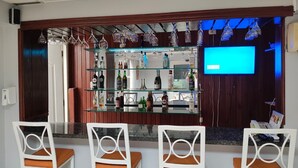 A bar area with three white chairs and a glass shelf displaying bottles and glasses. - Micro Hotel Condo Suites (Santo Domingo)