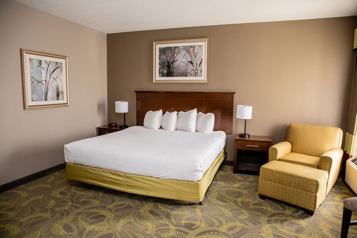 A hotel room with a large bed, a chair, two bedside tables, and two wall-mounted lamps.