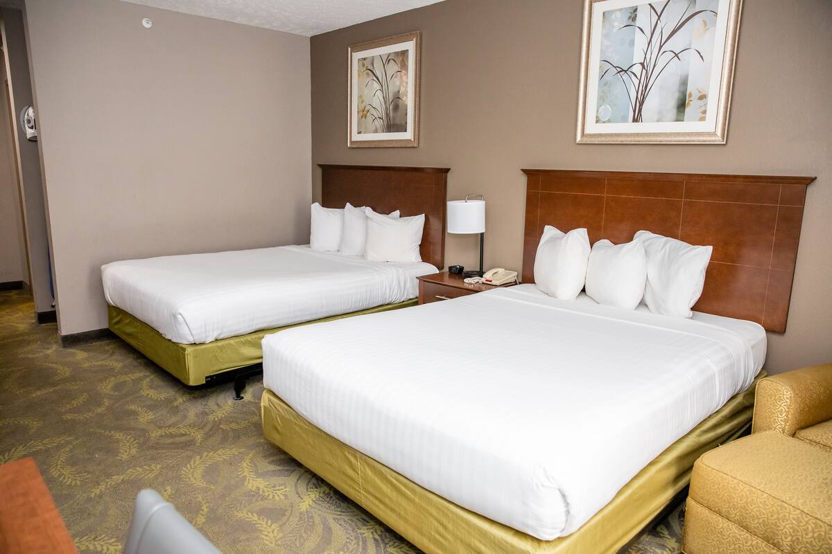 A hotel room with two beds, a nightstand with a lamp, and a chair.