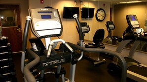 Kuntosali, jossa on useita erilaisia kuntoilulaitteita, kuten juoksumattoja ja crosstrainer, sekä peiliseinä ja kello.