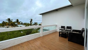 A balcony with a wooden floor, white railing, and two black chairs. - Hotel Cally Galapagos (Puerto Villamil)
