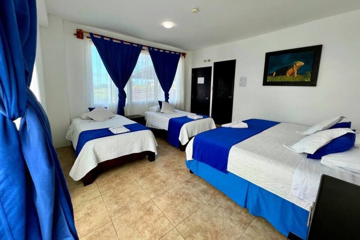 A hotel room with three beds, each with a blue and white bedspread, and a painting on the wall.