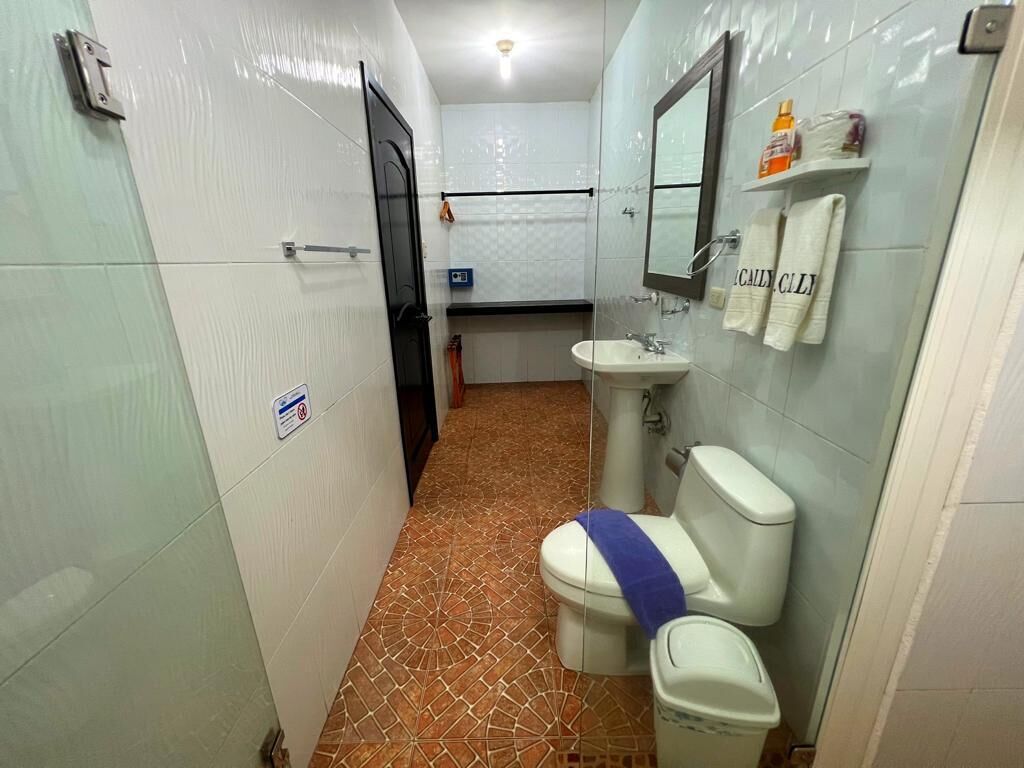 A bathroom with a toilet, sink, and mirror. There is a towel hanging on the wall and a sign on the door.