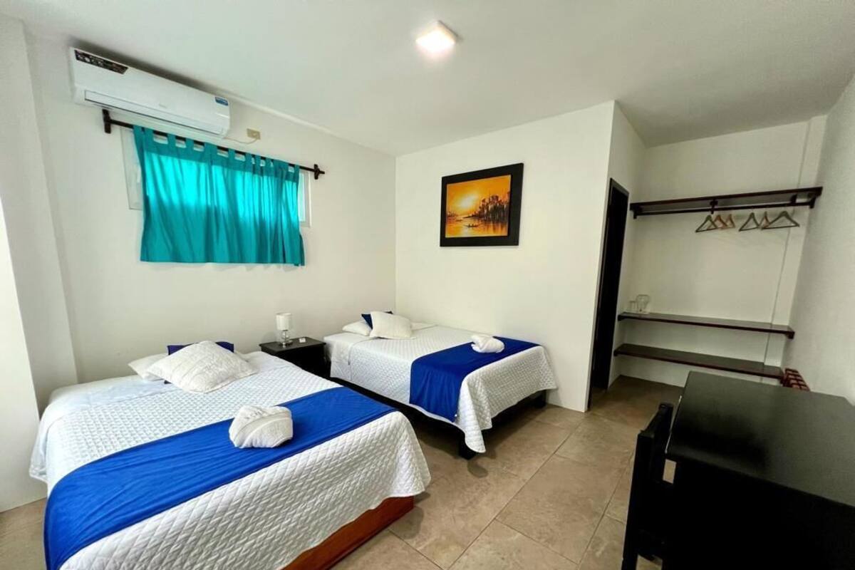 A hotel room with two beds, a desk, a chair, a painting on the wall, and a window with curtains.