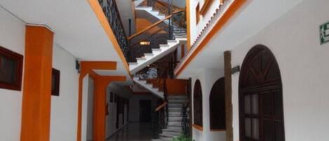 A corridor with a staircase leading to an upper level, featuring a tiled floor and wooden accents.