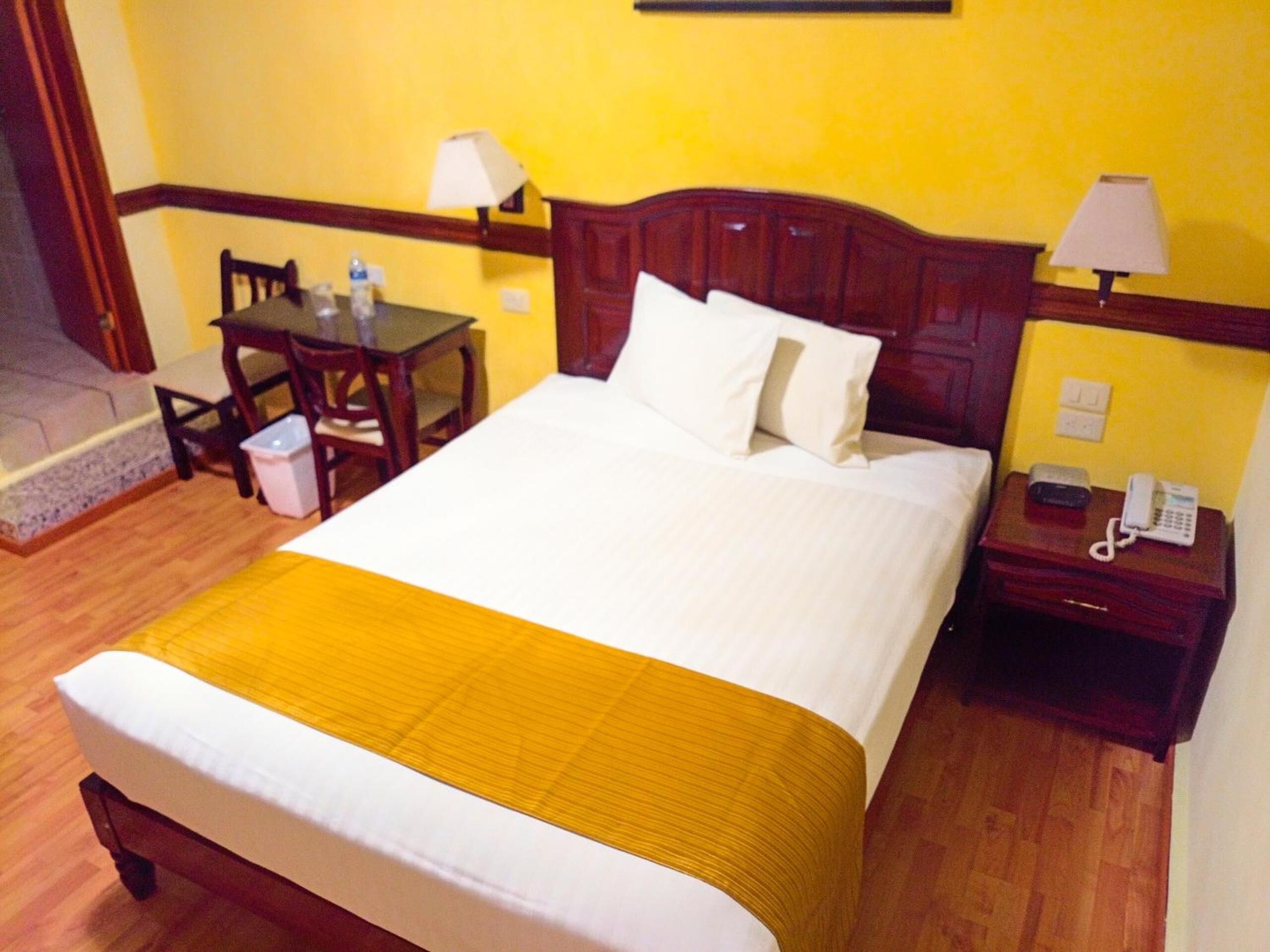 A hotel room with a bed, a desk, a chair, a lamp, and a telephone.