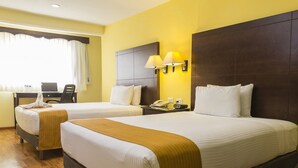 Habitación de hotel con dos camas, un escritorio, una computadora portátil, un teléfono y una ventana con cortinas.