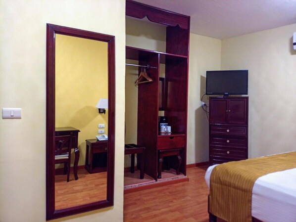 Une chambre d’hôtel avec une armoire en bois, un lit recouvert d’une couverture marron, un bureau avec une lampe et un téléviseur posé sur un meuble.
