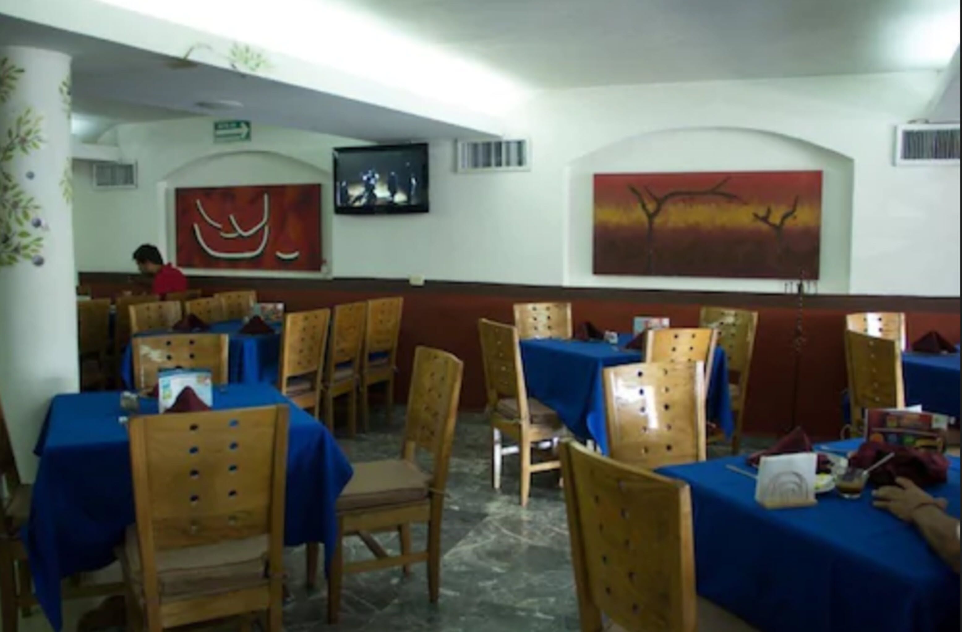A restaurant with wooden chairs and tables, a TV mounted on the wall, and artwork on the walls.
