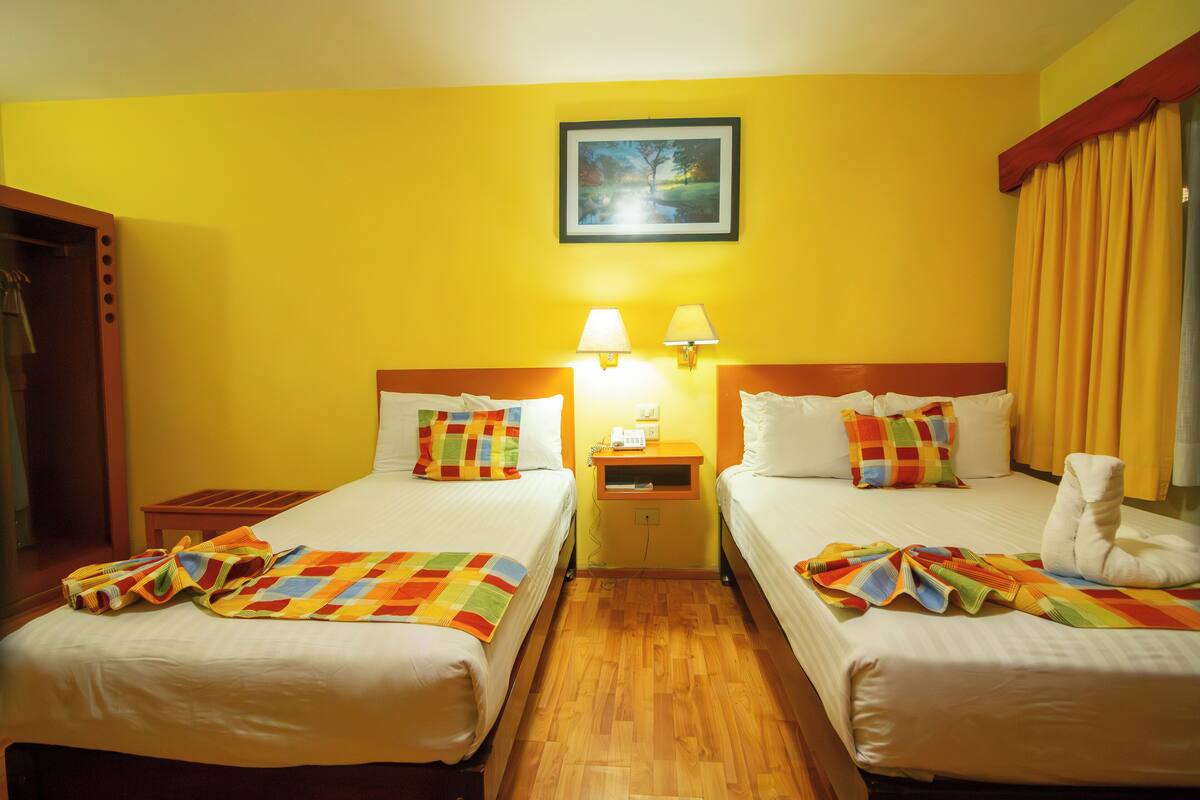 A hotel room with two beds, a nightstand with lamps, a painting on the wall, and a window with curtains.